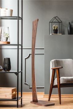 a wooden floor lamp next to a chair in a room with gray walls and shelves