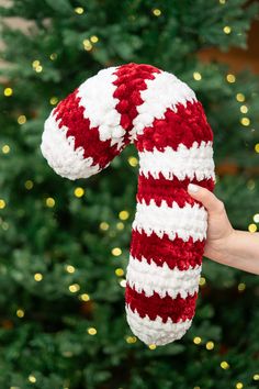 a hand holding a red and white knitted christmas stocking in front of a christmas tree