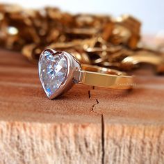 a heart shaped diamond ring sitting on top of a piece of wood