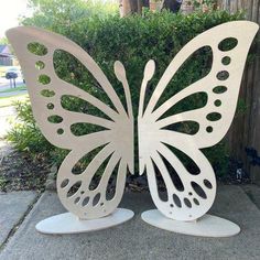 two white metal butterfly sculptures sitting on top of a cement ground next to a bush