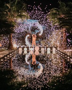 fireworks are lit up in the night sky above a fountain with people standing on it