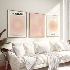 a living room filled with white furniture and paintings on the wall above it's couch