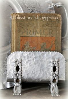 an old book sitting on top of a white table next to some silver vases