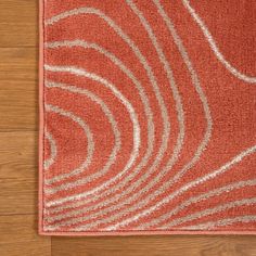 a red area rug with white swirls on the top and bottom, in front of a wooden floor