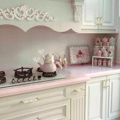 a kitchen with white cabinets and pink counter tops, including a tea kettle on the stove