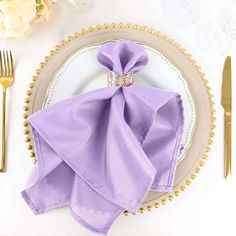 a place setting with purple napkins and silverware on a white table cloth covered plate