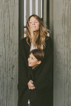 a woman and child standing next to each other in front of a wooden fence with their arms around each other