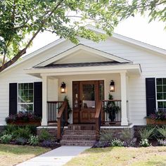 a small white house with black shutters and flowers on the front porch is shown