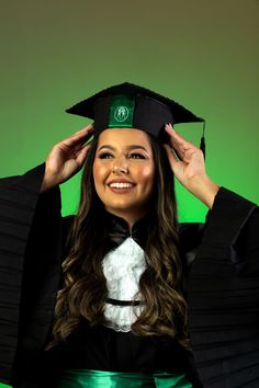 a woman in a graduation cap and gown smiles while holding her hands on her head