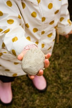 a person holding a rock in their hand on the grass with yellow dots all over them