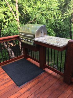 an outdoor grill on a deck in front of some trees and grass with a black doormat