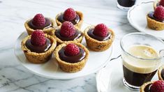 small desserts with chocolate and raspberries are on white plates next to a cup of coffee