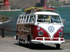 a red and white vw bus parked on the side of the road near the ocean