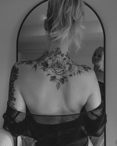 a woman with a flower tattoo on her back is looking at herself in the mirror