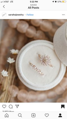 two rings are sitting on top of a white box with some flowers in the background