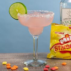 a pink drink with a lime garnish and candy on the table next to it