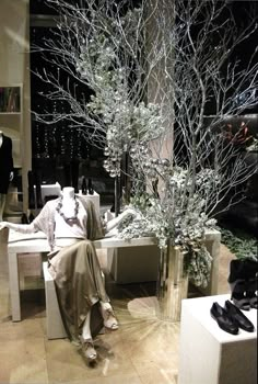 a woman sitting on a bench next to a vase with trees in it and other mannequins