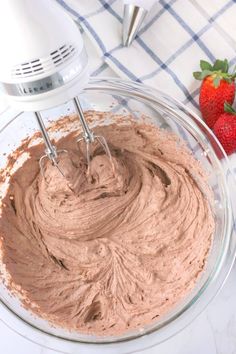 a bowl filled with chocolate frosting next to strawberries