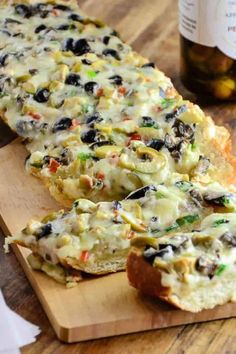 two pieces of bread on a cutting board with olives and cheese