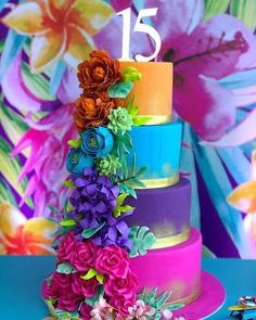 a multi - tiered cake with colorful flowers on the top and bottom is displayed in front of a floral backdrop