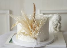 there is a white cake with feathers on it and a book next to the cake