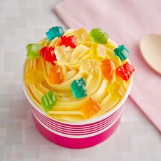 a cupcake with gummy bears in it on a pink plate next to a spoon