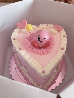 a heart shaped cake in a box with a pink and white decoration on it's side