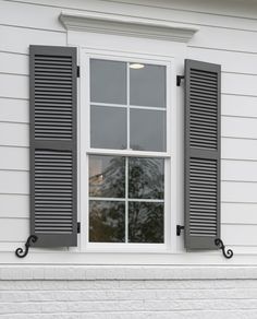 an open window with black shutters on the side of a white brick building,