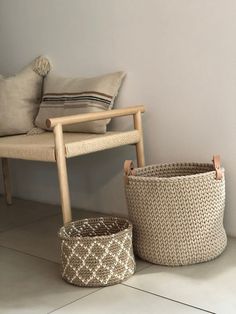 two baskets sitting next to each other on the floor near a chair with pillows in it