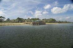 a pier on the water with trees in the background and clouds in the sky above