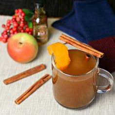 a glass mug with cinnamon sticks sticking out of it and an apple in the background