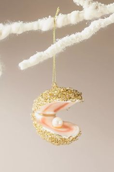 an ornament hanging from a tree branch with pearls and gold glitter on it