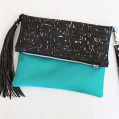 a black and teal clutch bag with tassels on the front, sitting on a white surface