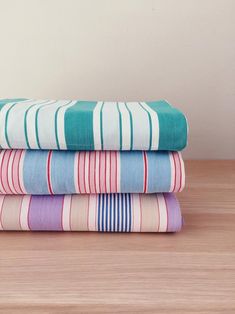 three folded towels sitting on top of a wooden table next to each other in different colors