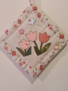 an embroidered square with pink flowers and a butterfly on it is hanging from a hook