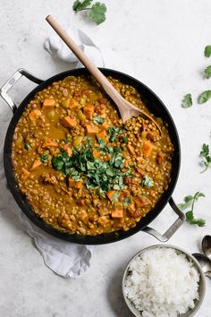 a pan filled with lentils and rice next to a wooden spoon on a white surface