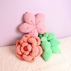 three pink and green flowers sitting on top of a white blanket next to a wall