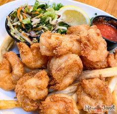 fried shrimp and french fries on a white plate with coleslaw, lettuce, and dipping sauce