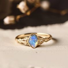 a gold ring with an opal stone in the center on a white surface next to flowers