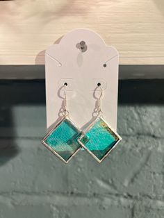 a pair of earrings with green and blue squares hanging from it's earwires