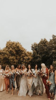 a group of women standing next to each other holding bouquets in their hands and wearing dresses