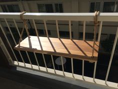 a wooden swing hanging from the side of a balcony next to a building with white balconies