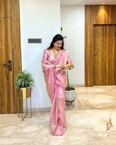 a woman in a pink sari is looking at her cell phone while standing next to a potted plant