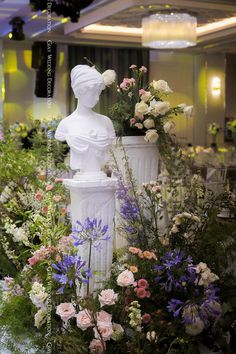 a white statue surrounded by flowers and greenery