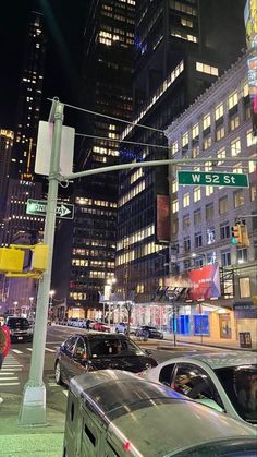 cars are stopped at an intersection on a busy city street in the night time, with skyscrapers lit up behind them