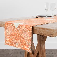 an orange and white table runner on top of a wooden table with two wine glasses