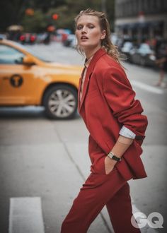 a woman in a red suit is walking down the street with her hand on her hip