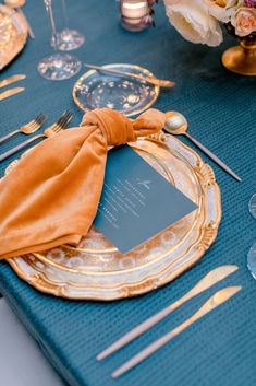 a blue table cloth and gold plates with napkins on it, along with silverware