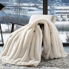 a chair with a blanket on top of it in front of a window overlooking the snow covered ground