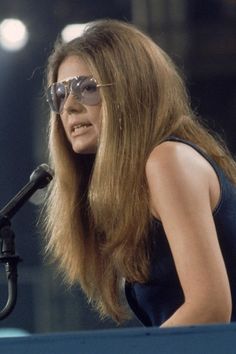 a woman with sunglasses on sitting in front of a microphone